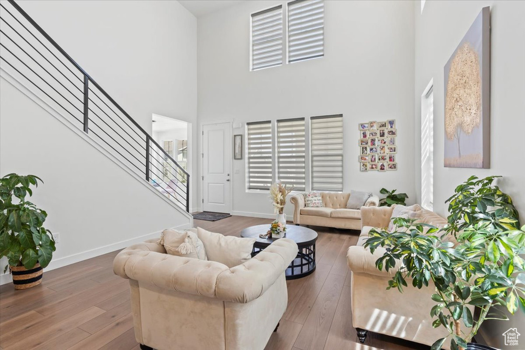 Living area with a high ceiling, stairs, wood-type flooring, and plenty of natural light