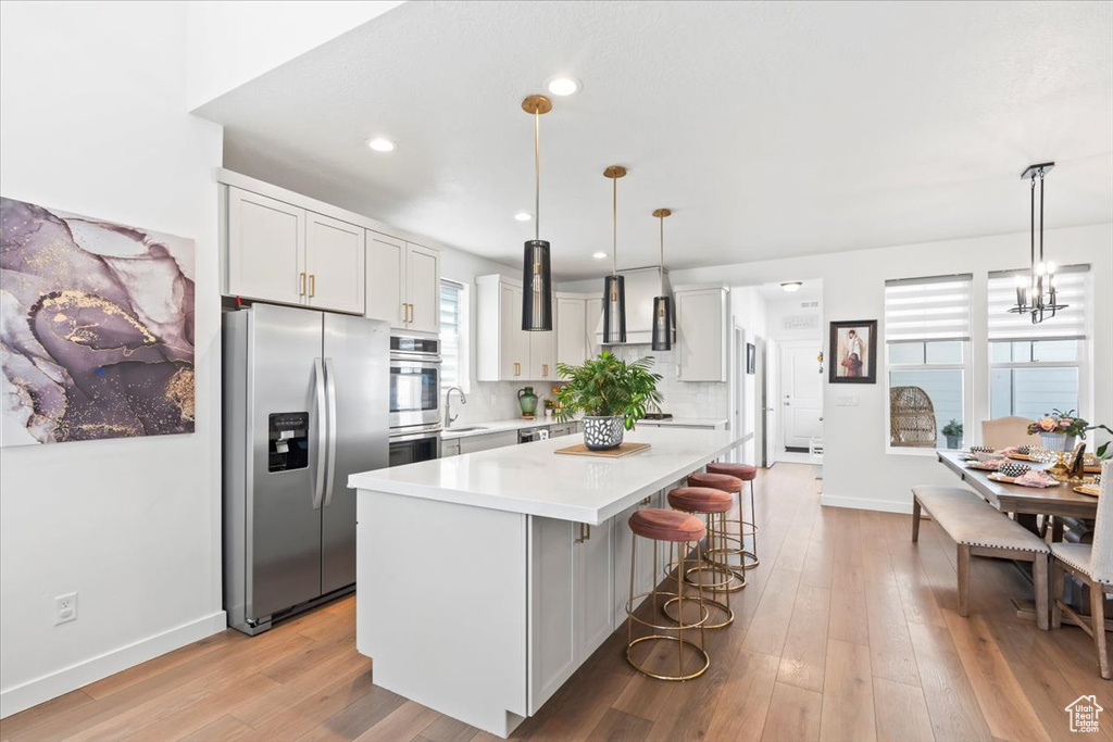 Kitchen with stainless steel refrigerator with ice dispenser, light countertops, a kitchen bar, a center island, and light wood-style floors