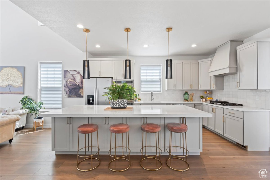 Kitchen featuring premium range hood, stainless steel appliances, a kitchen island, decorative backsplash, and a breakfast bar area