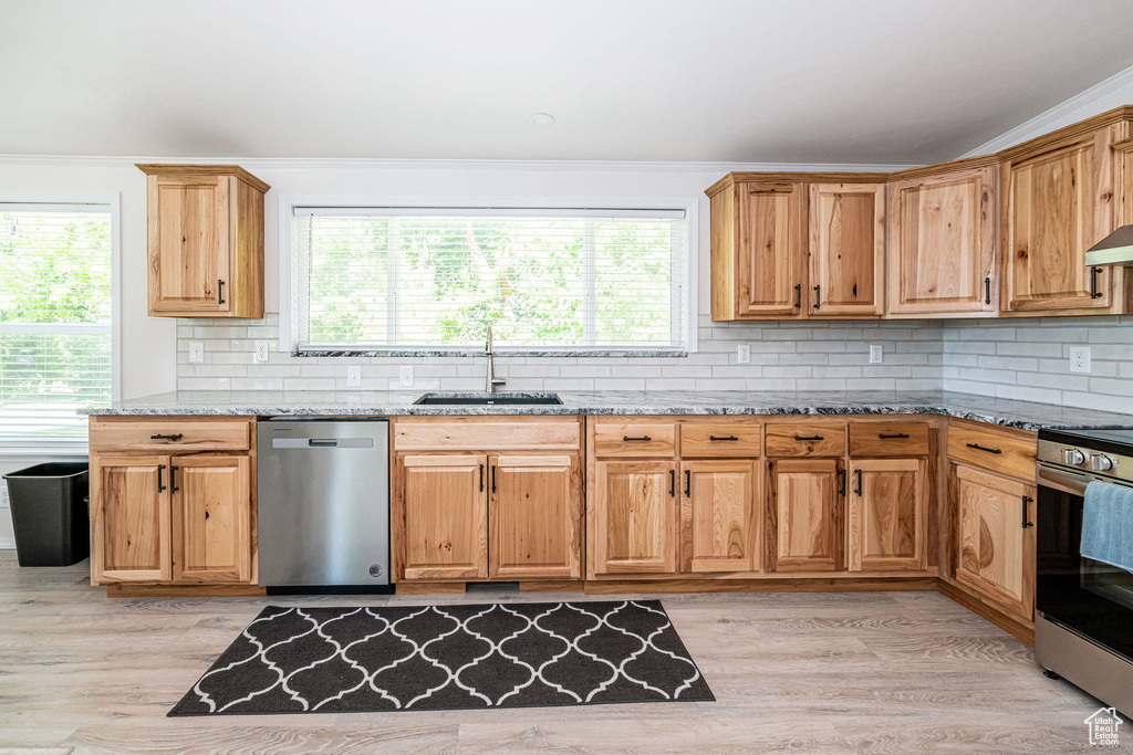 Kitchen featuring stainless steel appliances, light stone countertops, light wood-style flooring, healthy amount of natural light, and crown molding