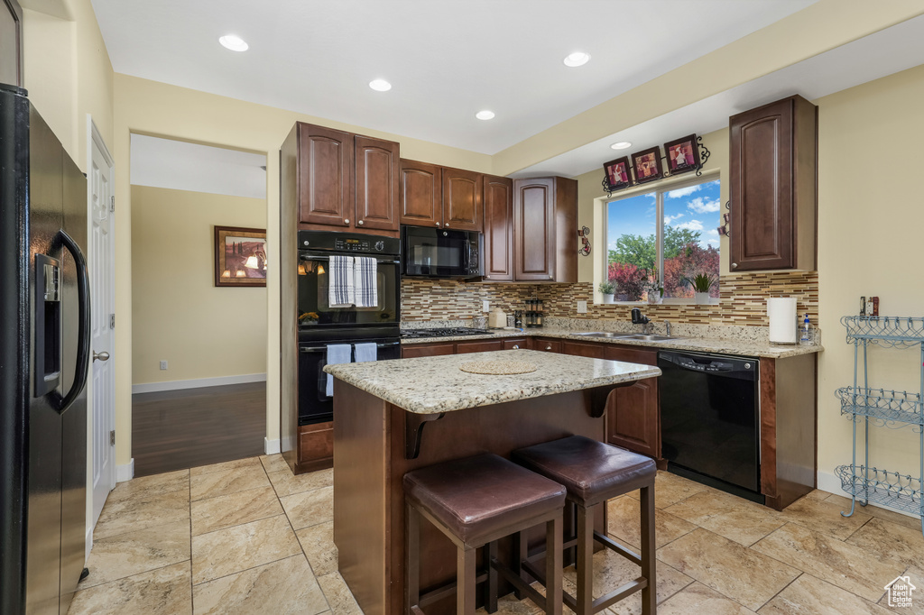 Kitchen featuring black appliances, decorative backsplash, a kitchen breakfast bar, light stone countertops, and a center island
