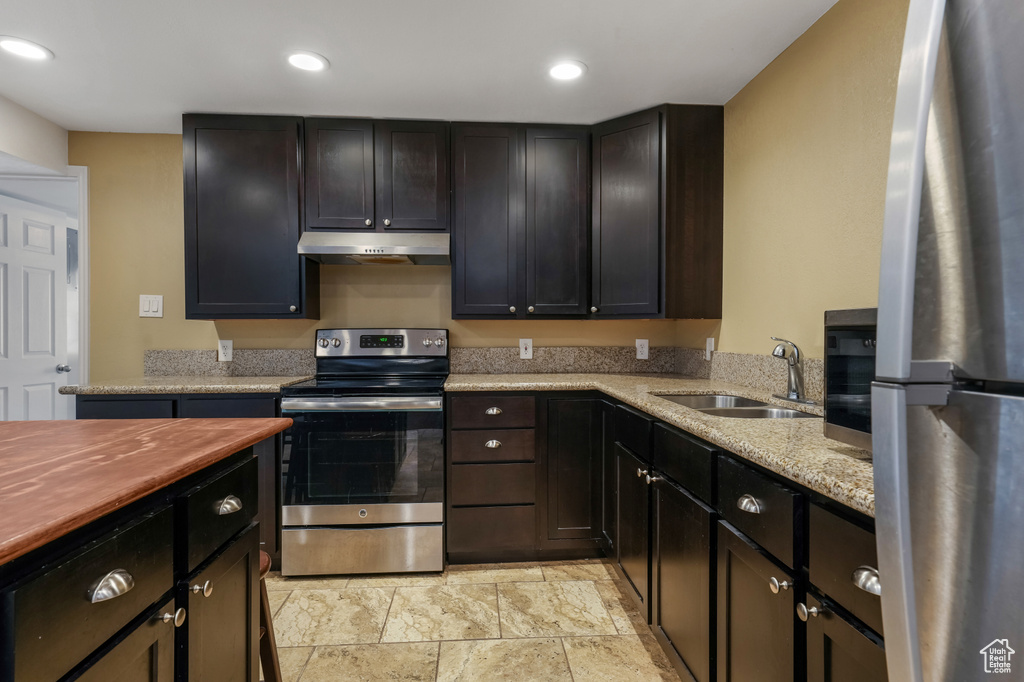 Kitchen featuring appliances with stainless steel finishes, under cabinet range hood, butcher block countertops, recessed lighting, and light stone finish floors