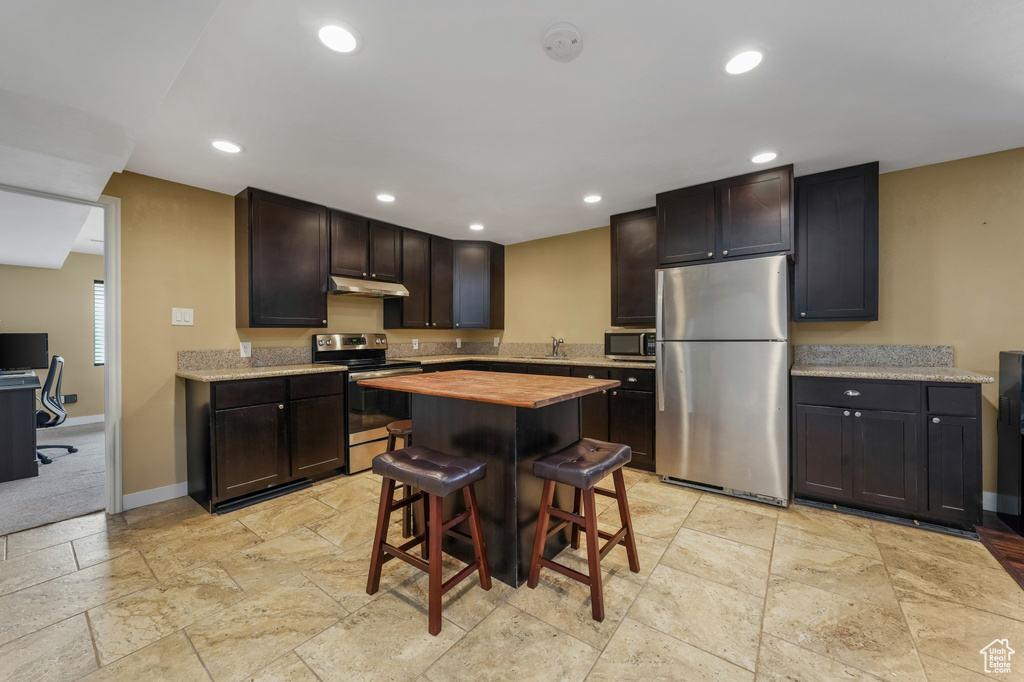 Kitchen featuring stainless steel appliances, under cabinet range hood, butcher block counters, recessed lighting, and stone tile flooring