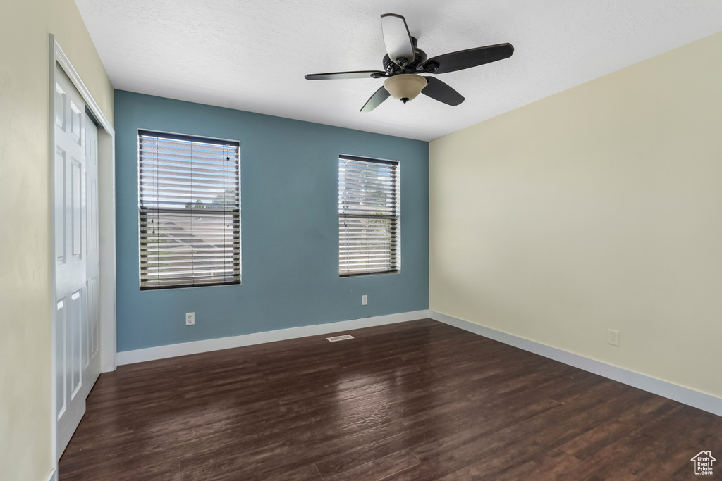 Unfurnished bedroom with a closet, dark wood-style flooring, and a ceiling fan