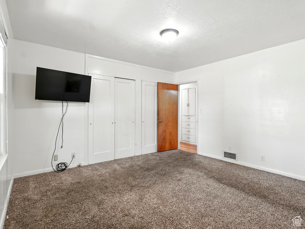 Unfurnished bedroom with carpet, a textured ceiling, and a closet