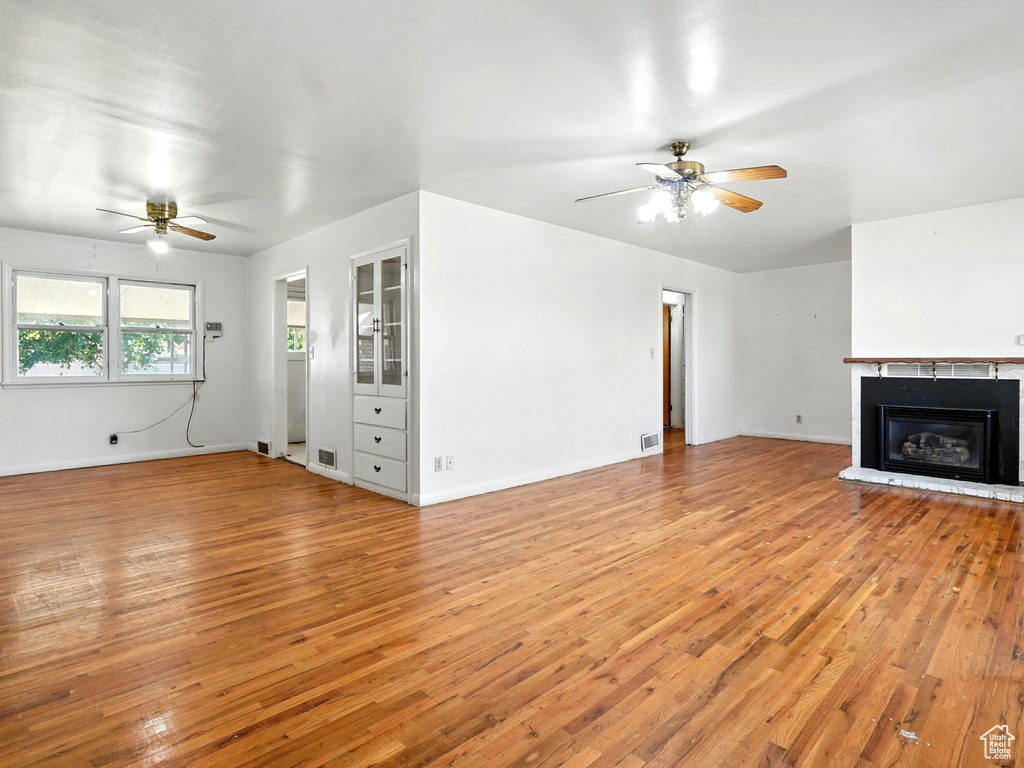 Unfurnished living room with ceiling fan, light wood finished floors, and a glass covered fireplace