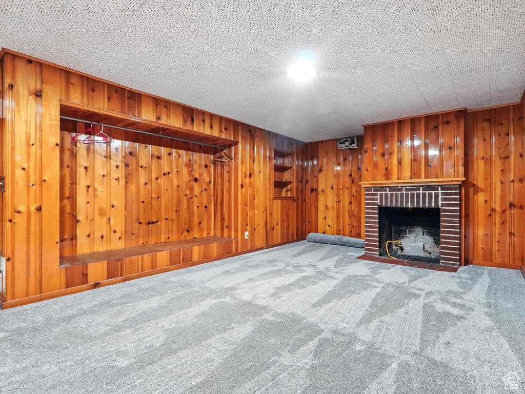 Unfurnished living room featuring carpet floors, wood walls, and a fireplace