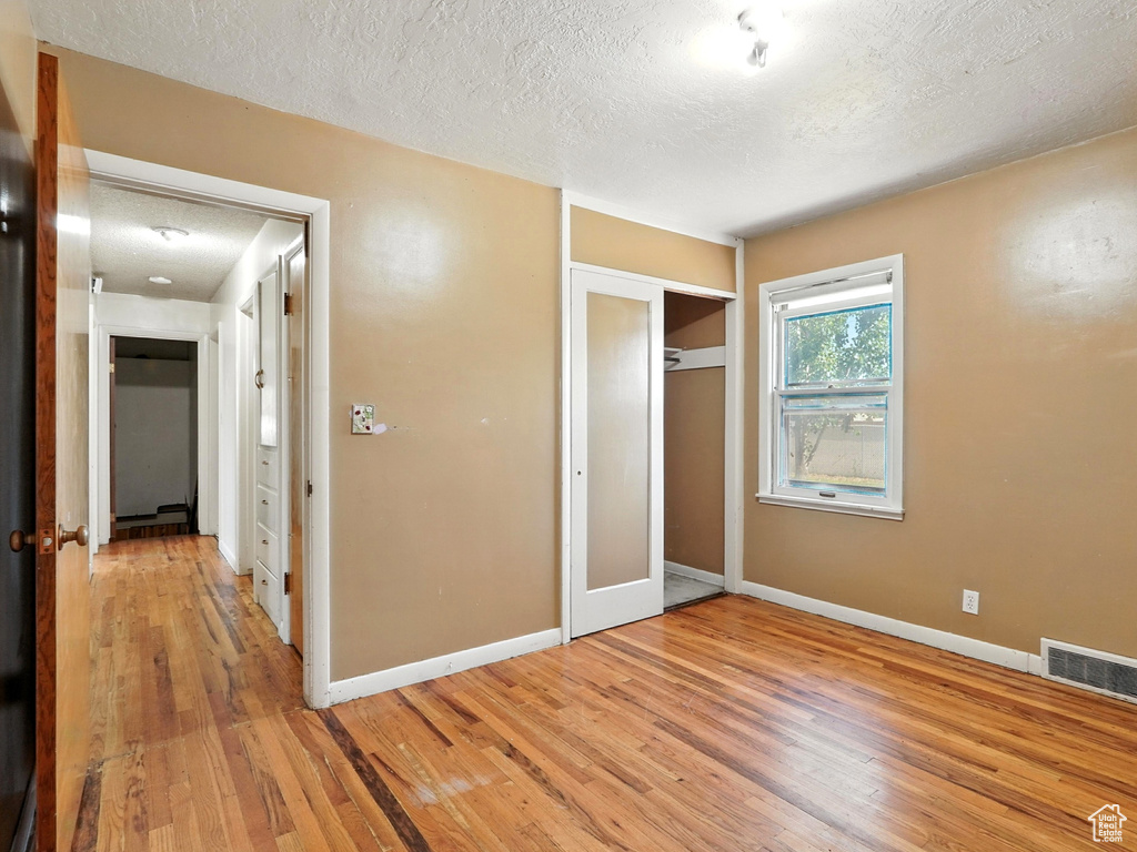 Unfurnished bedroom featuring a textured ceiling, light wood-type flooring, and a closet
