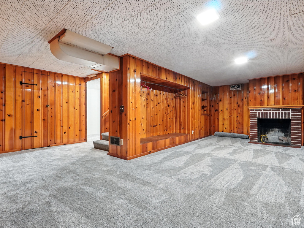 Finished basement featuring carpet floors, a brick fireplace, wooden walls, and stairs