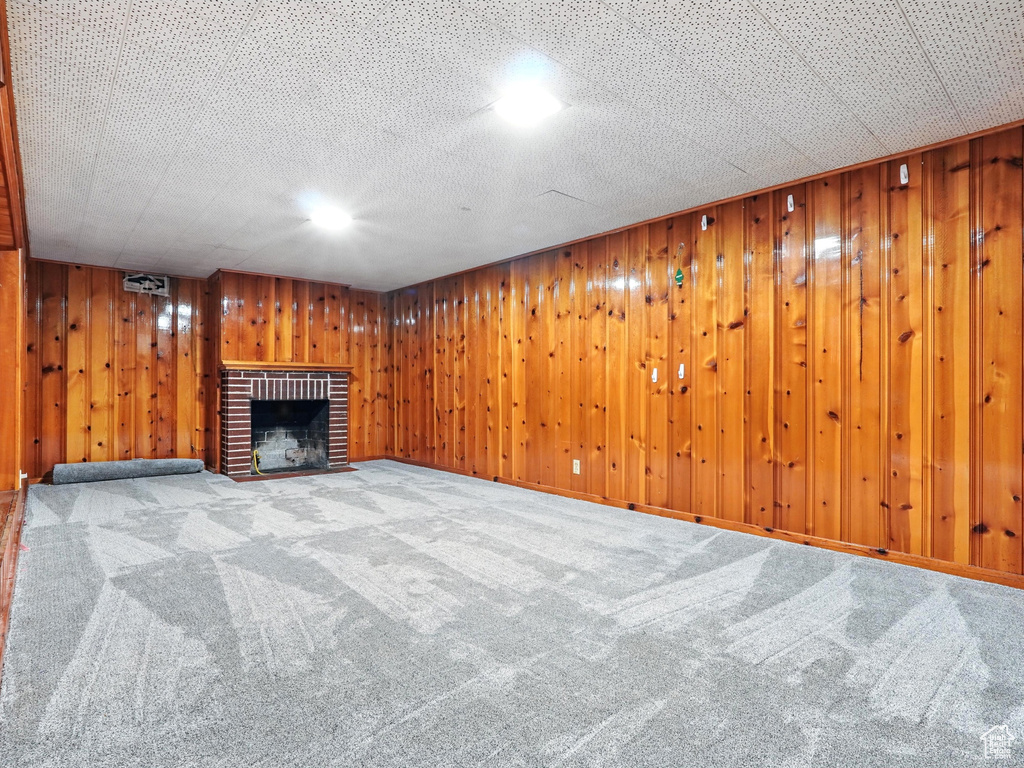 Unfurnished living room with a fireplace, carpet flooring, and wood walls