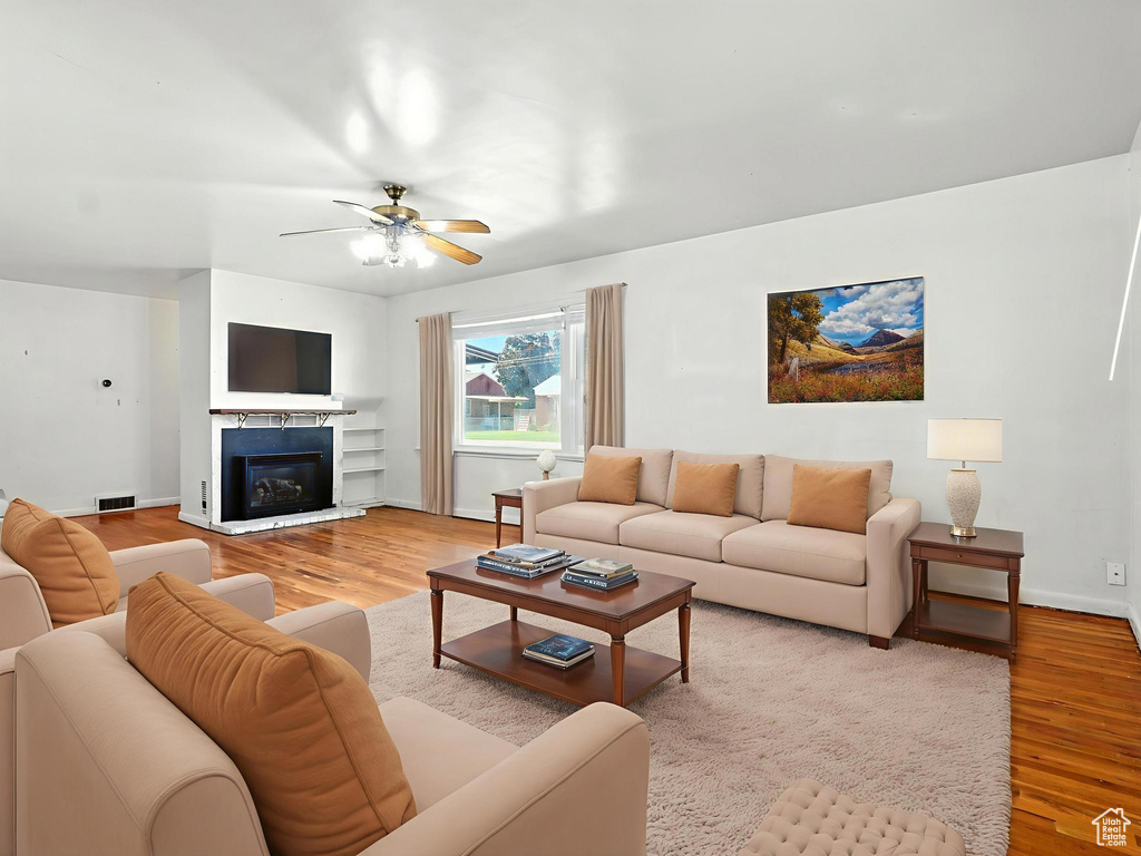 Living area featuring light wood finished floors, a ceiling fan, and a glass covered fireplace