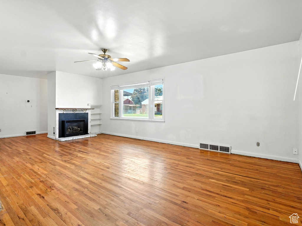 Unfurnished living room with light wood finished floors, a glass covered fireplace, and ceiling fan