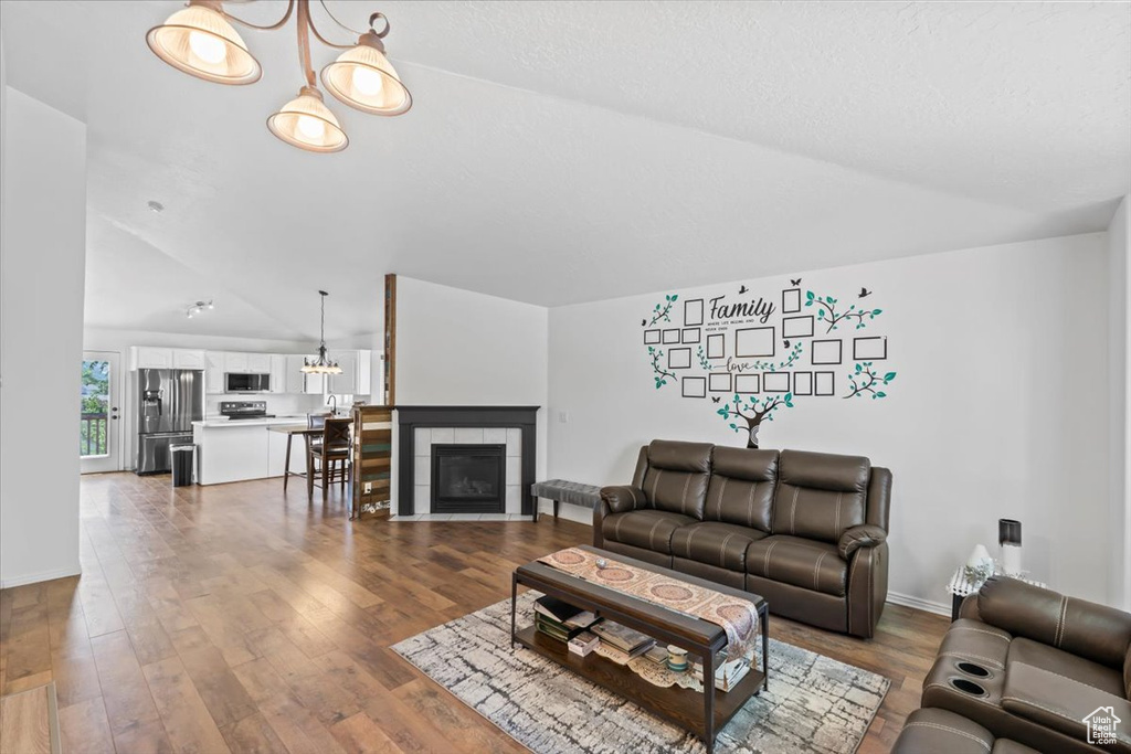 Living area with vaulted ceiling, wood finished floors, a tile fireplace, and a chandelier