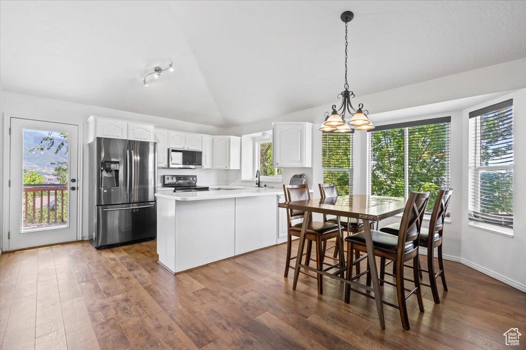 Kitchen featuring stainless steel appliances, white cabinetry, hardwood / wood-style floors, a chandelier, and vaulted ceiling