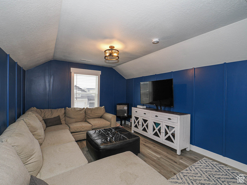 Living room with a textured ceiling, lofted ceiling, and wood finished floors