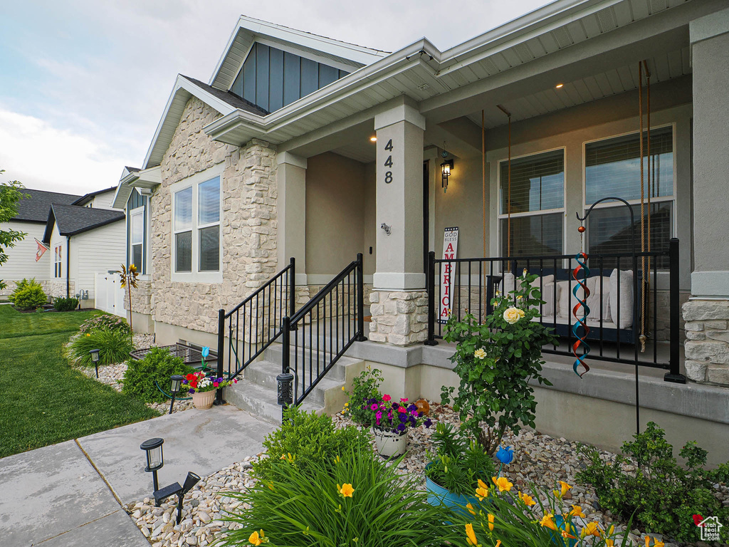 Doorway to property featuring stone siding, board and batten siding, covered porch, and stucco siding