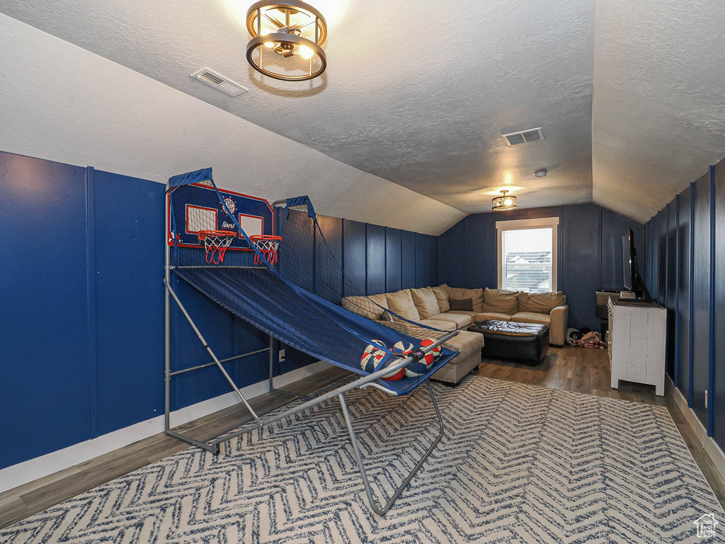 Recreation room with a textured ceiling, wood finished floors, and lofted ceiling