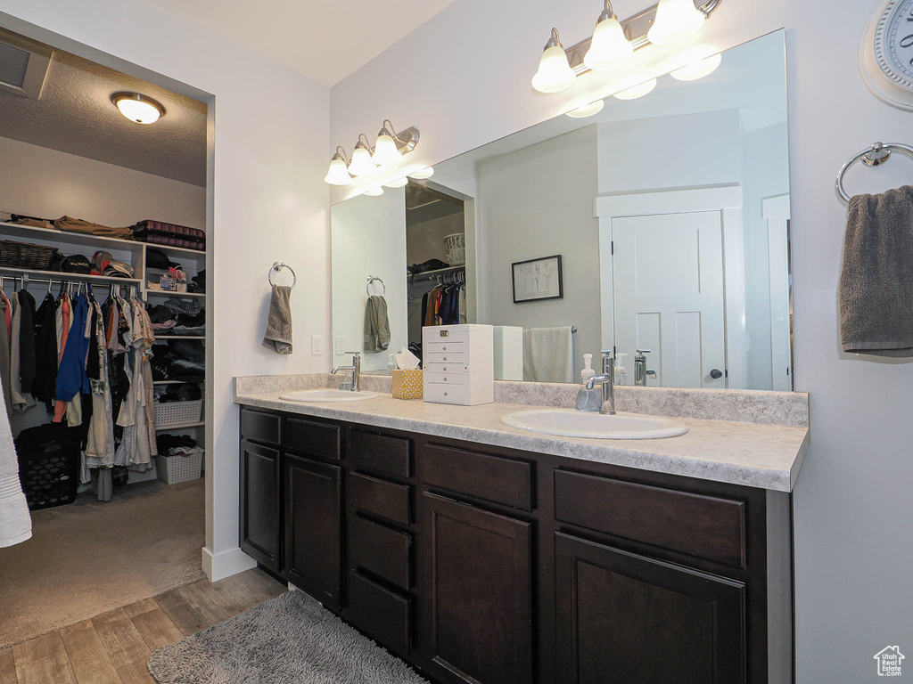Full bath with double vanity, a spacious closet, and wood finished floors