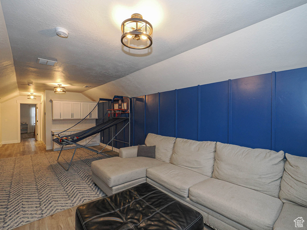 Living area with light wood finished floors, vaulted ceiling, a textured ceiling, and a decorative wall