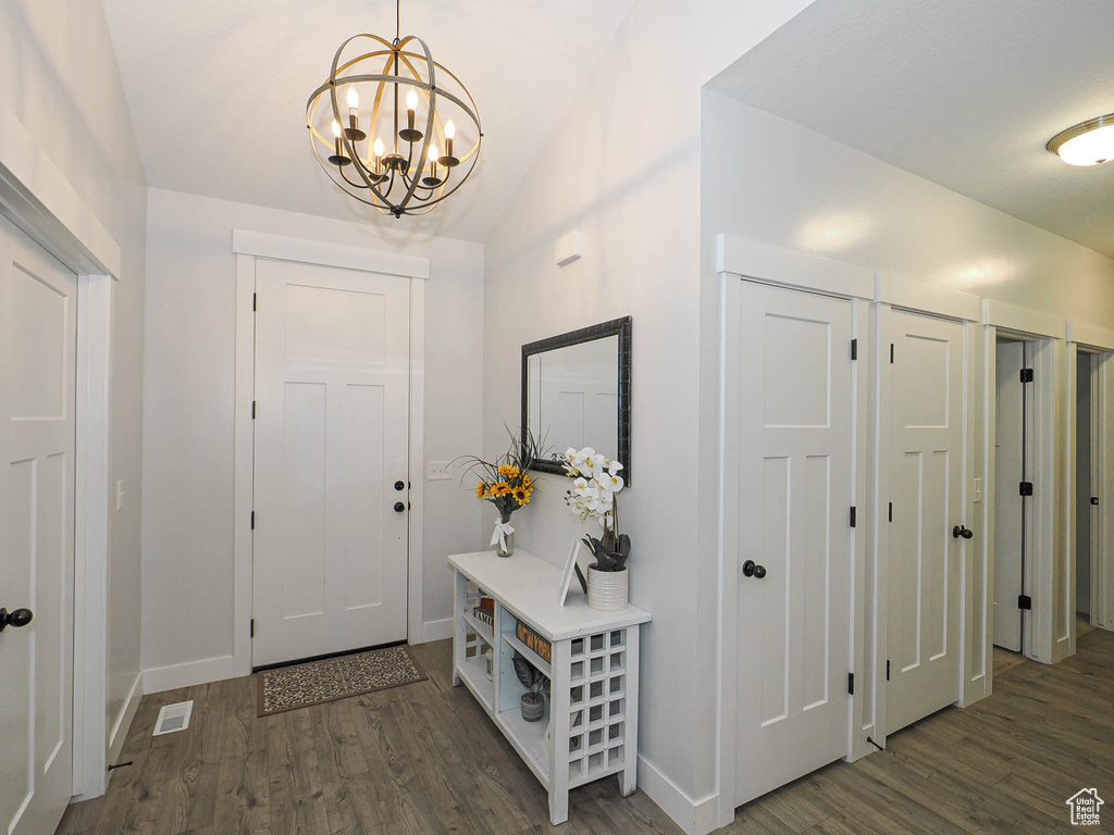 Entryway with dark wood-type flooring, a chandelier, and lofted ceiling