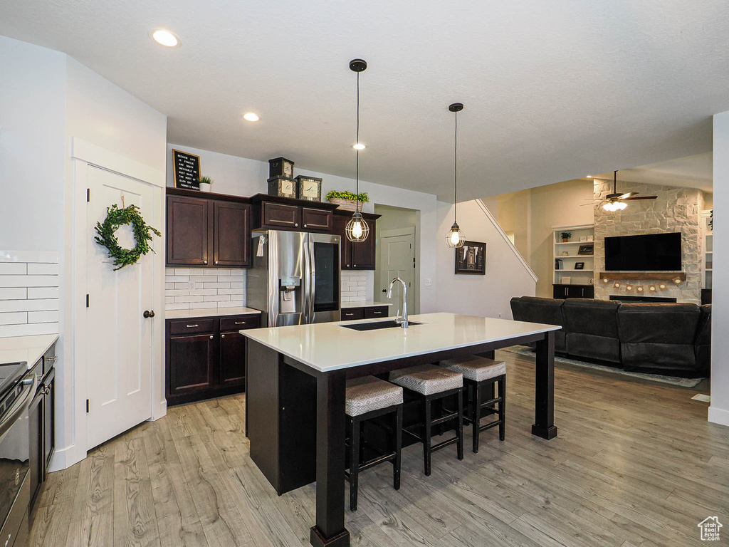 Kitchen with stainless steel refrigerator with ice dispenser, a ceiling fan, light wood-style flooring, a breakfast bar area, and tasteful backsplash
