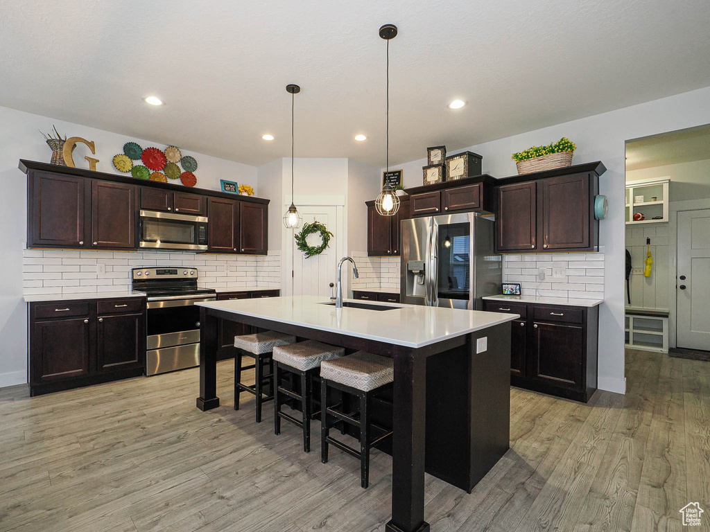 Kitchen with appliances with stainless steel finishes, light wood-type flooring, a breakfast bar, tasteful backsplash, and recessed lighting