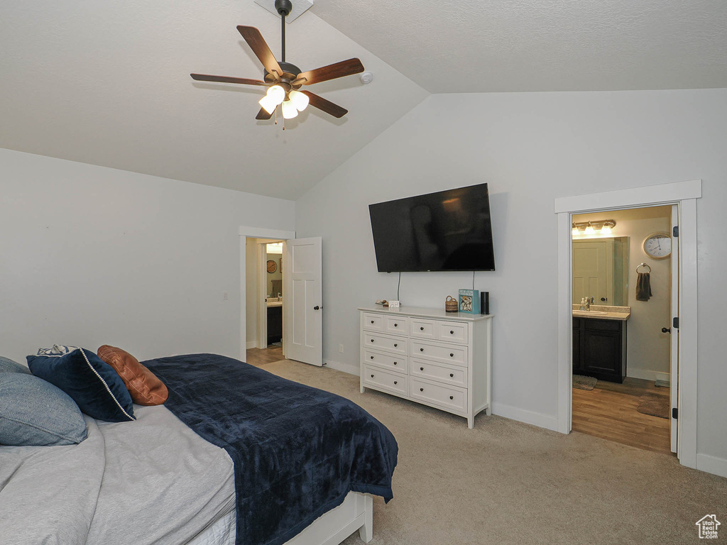 Bedroom with vaulted ceiling, light colored carpet, connected bathroom, and a ceiling fan