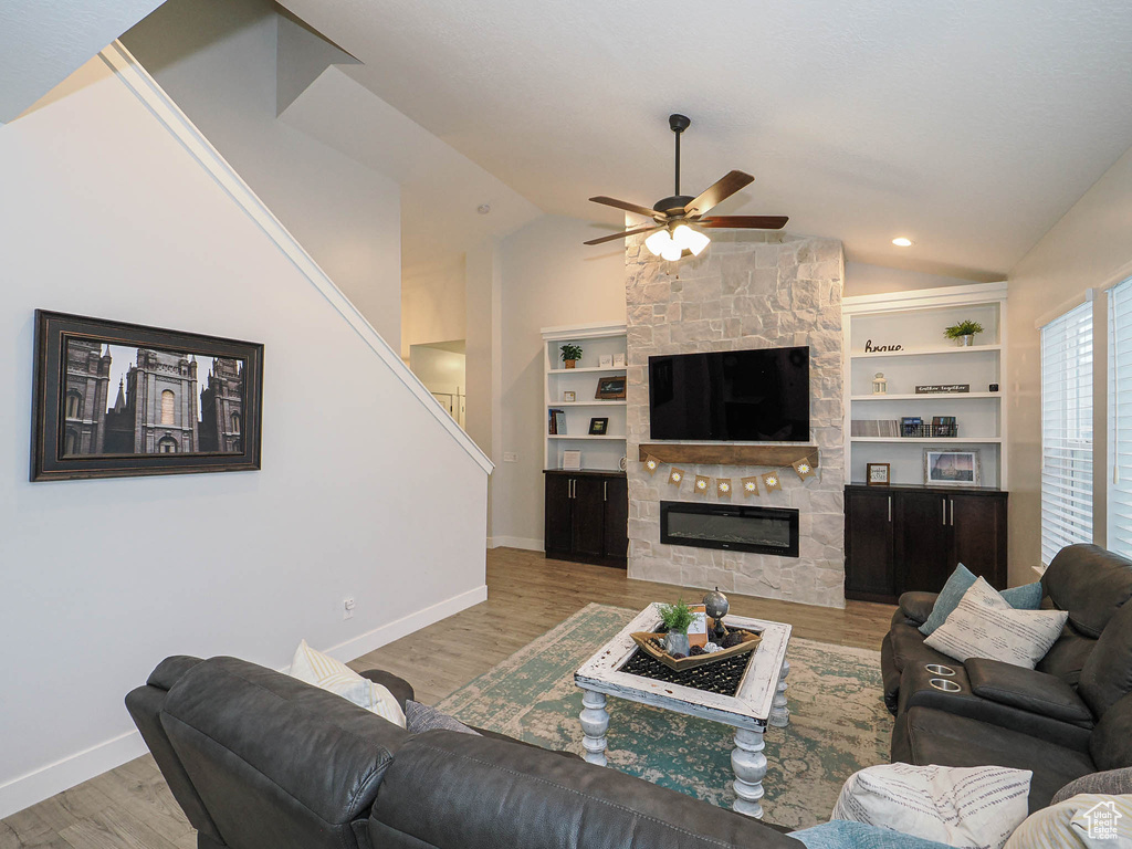 Living area with vaulted ceiling, ceiling fan, wood finished floors, a fireplace, and stairs