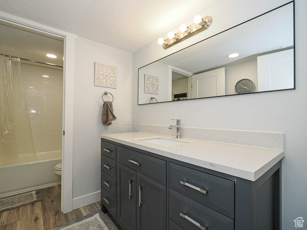 Full bathroom featuring wood finished floors, vanity, shower / bath combo with shower curtain, a textured ceiling, and recessed lighting
