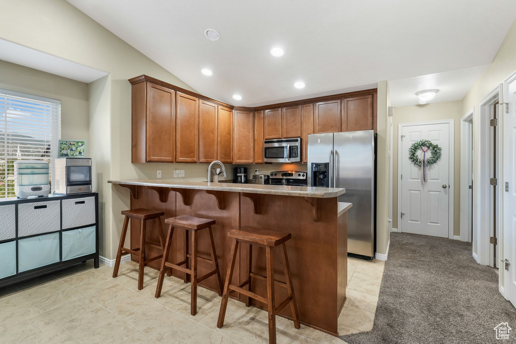 Kitchen featuring appliances with stainless steel finishes, a peninsula, brown cabinetry, a breakfast bar area, and recessed lighting