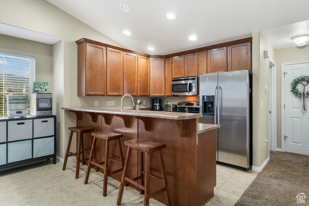 Kitchen with appliances with stainless steel finishes, a peninsula, a kitchen bar, brown cabinets, and recessed lighting