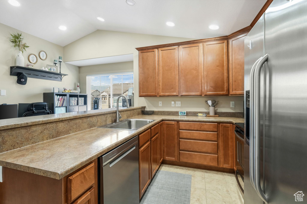 Kitchen featuring appliances with stainless steel finishes, vaulted ceiling, brown cabinetry, recessed lighting, and a peninsula