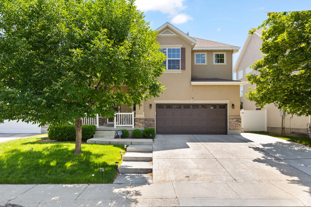 View of front facade featuring stucco siding, an attached garage, concrete driveway, and stone siding