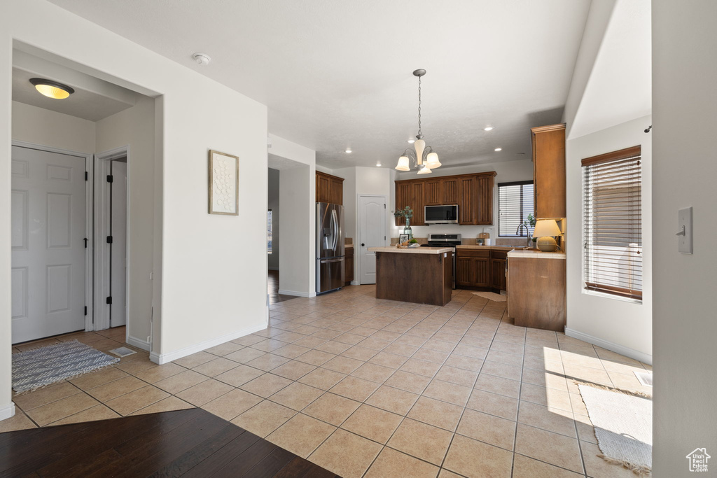 Kitchen featuring appliances with stainless steel finishes, a center island, light tile patterned floors, a chandelier, and light countertops