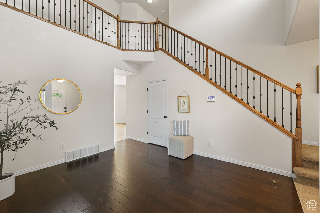 Unfurnished living room with hardwood / wood-style flooring, stairway, and a towering ceiling