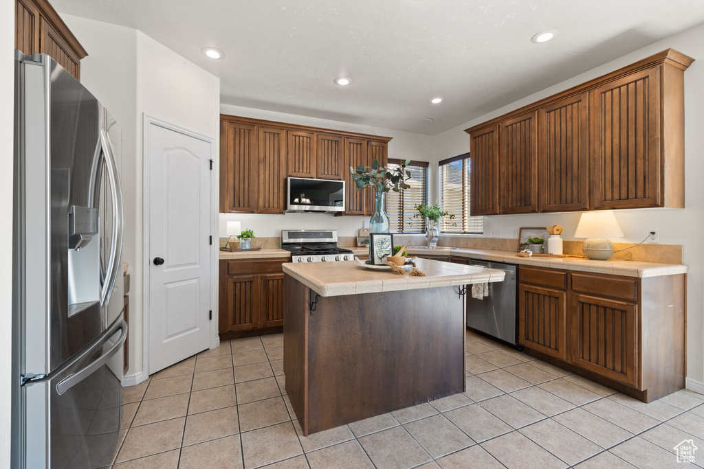 Kitchen with stainless steel appliances, tile countertops, recessed lighting, light tile patterned floors, and a kitchen island