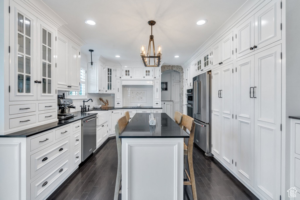 Kitchen with appliances with stainless steel finishes, dark countertops, a chandelier, white cabinetry, and a center island