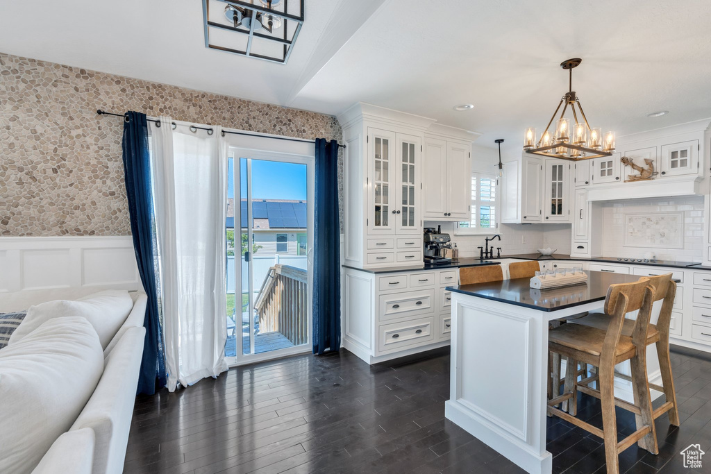 Kitchen featuring dark countertops, a chandelier, open floor plan, a wainscoted wall, and dark wood-style flooring