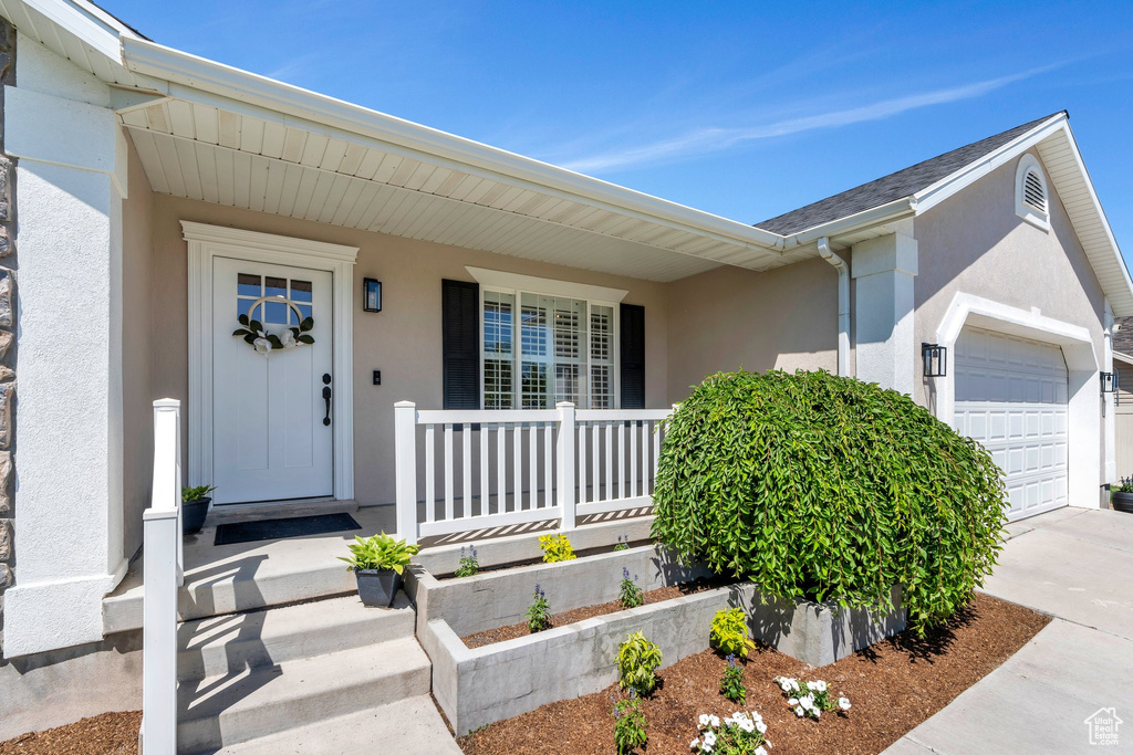 View of exterior entry featuring stucco siding, a porch, a garage, and concrete driveway