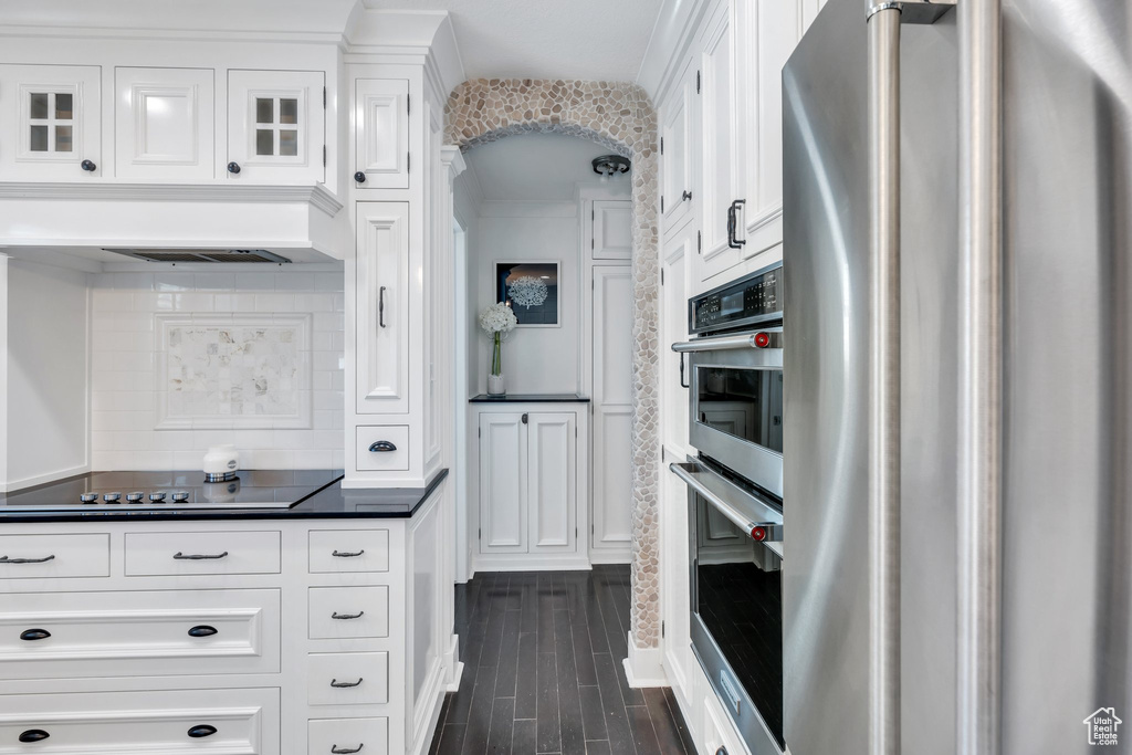 Kitchen featuring appliances with stainless steel finishes, dark countertops, white cabinets, backsplash, and dark wood-type flooring