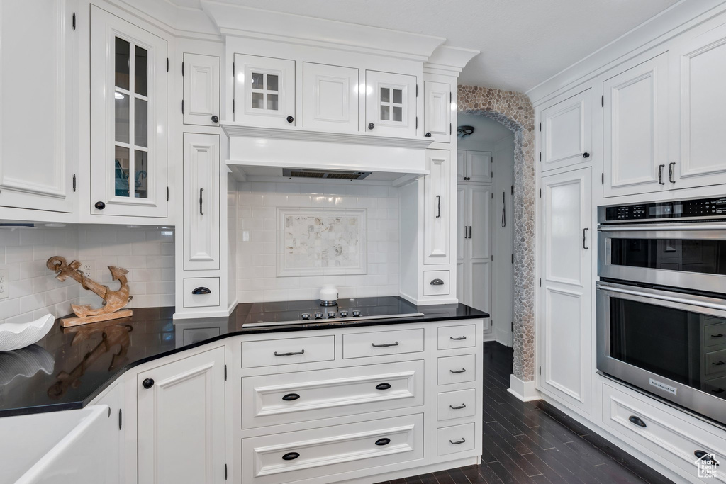 Kitchen featuring black electric stovetop, stainless steel double oven, white cabinetry, and glass insert cabinets