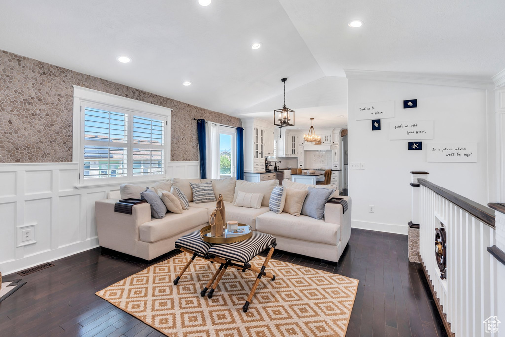 Living area featuring a wainscoted wall, wallpapered walls, vaulted ceiling, a chandelier, and dark wood finished floors