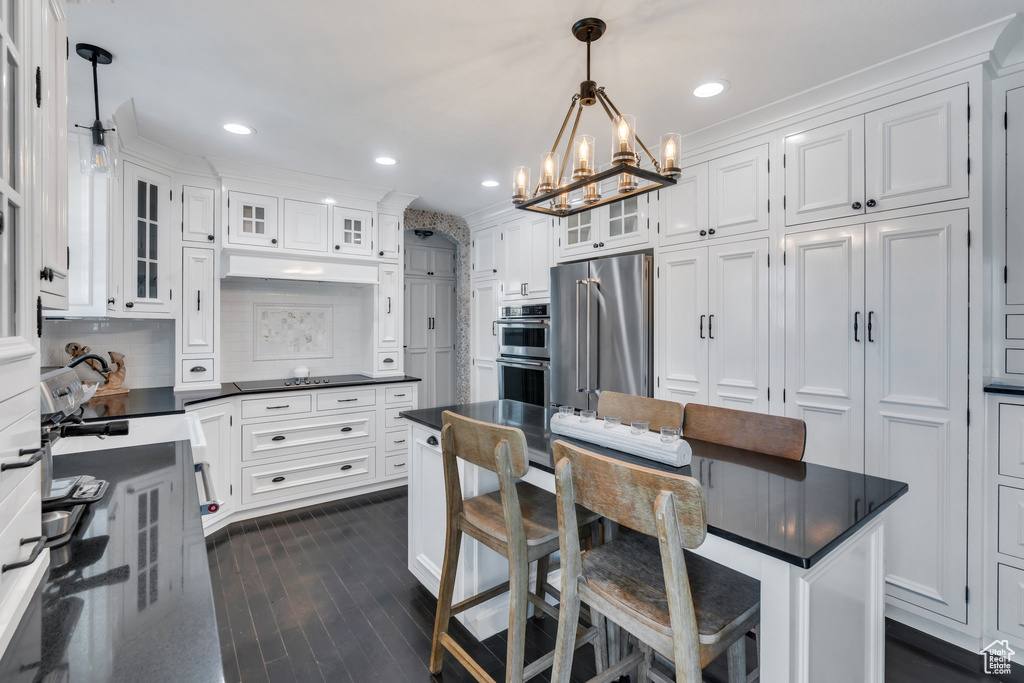 Kitchen featuring stainless steel appliances, a chandelier, white cabinets, dark countertops, and dark wood-type flooring