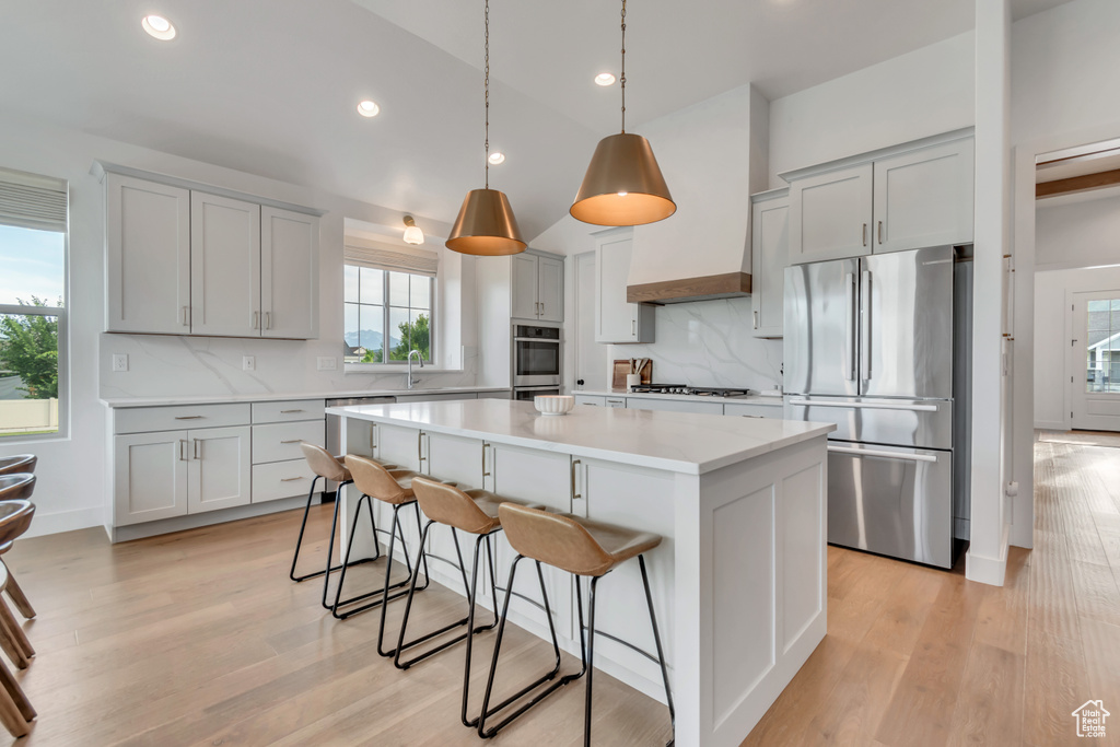Kitchen featuring appliances with stainless steel finishes, gray cabinets, a breakfast bar, a center island, and decorative backsplash