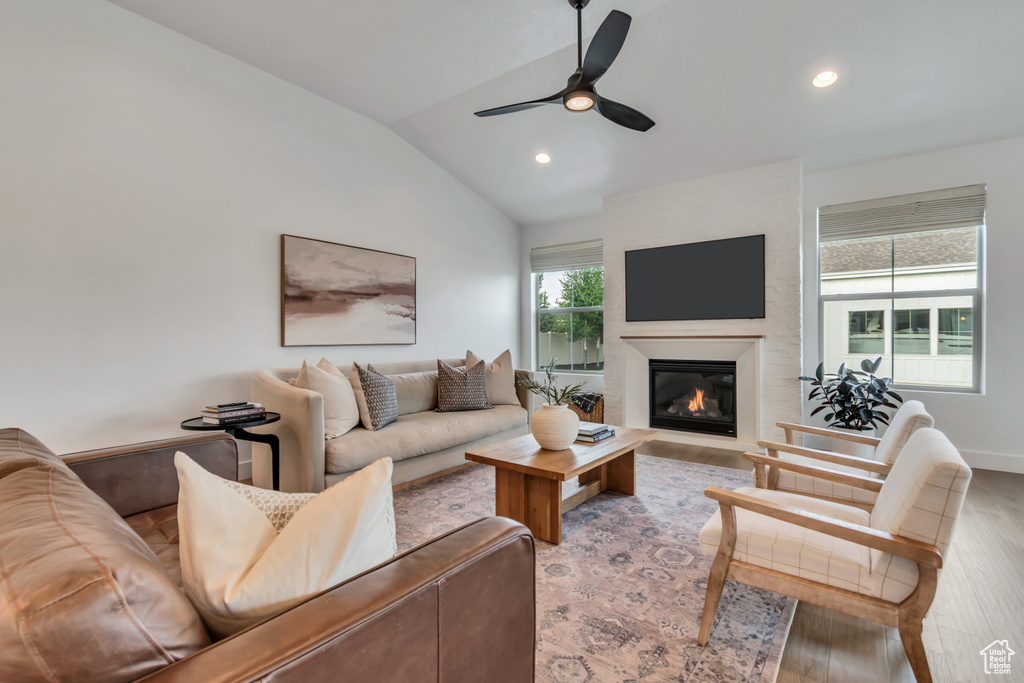Living room with wood finished floors, lofted ceiling, a glass covered fireplace, a ceiling fan, and recessed lighting