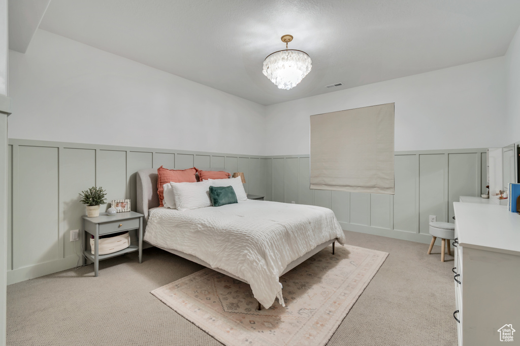 Bedroom with light carpet, a decorative wall, a chandelier, and wainscoting