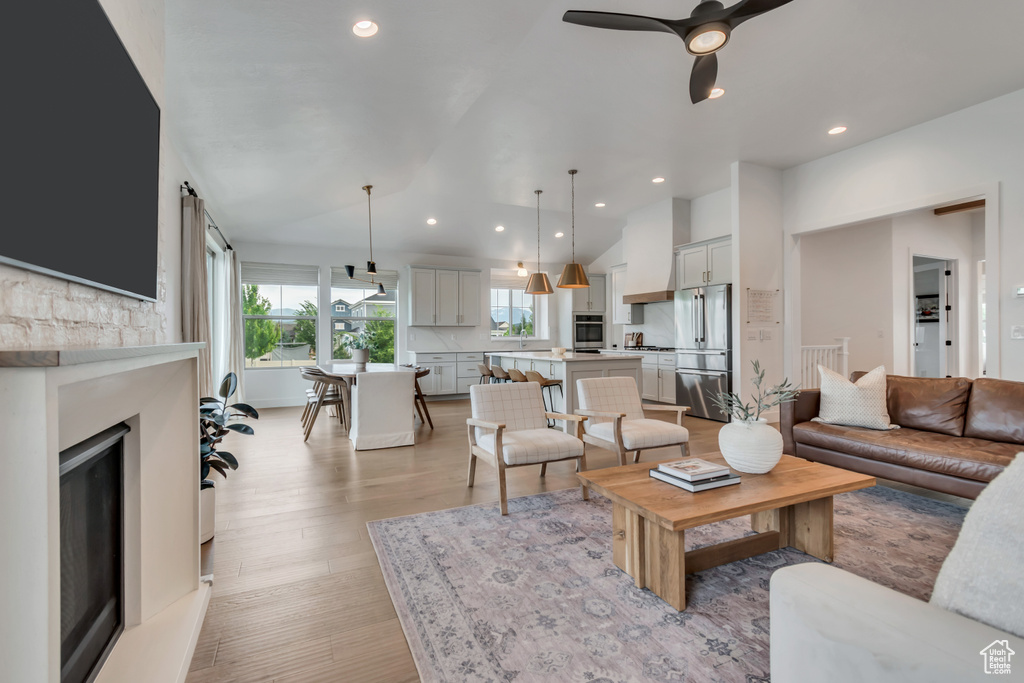 Living room featuring vaulted ceiling, light wood-style floors, recessed lighting, a fireplace with raised hearth, and ceiling fan