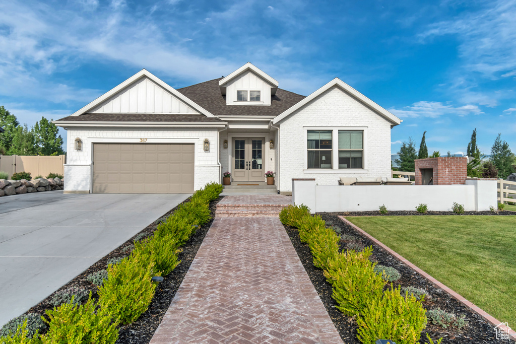 View of front of home with french doors, driveway, brick siding, a garage, and board and batten siding