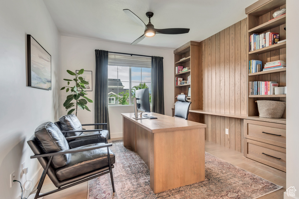 Home office with ceiling fan, wooden walls, and light wood finished floors