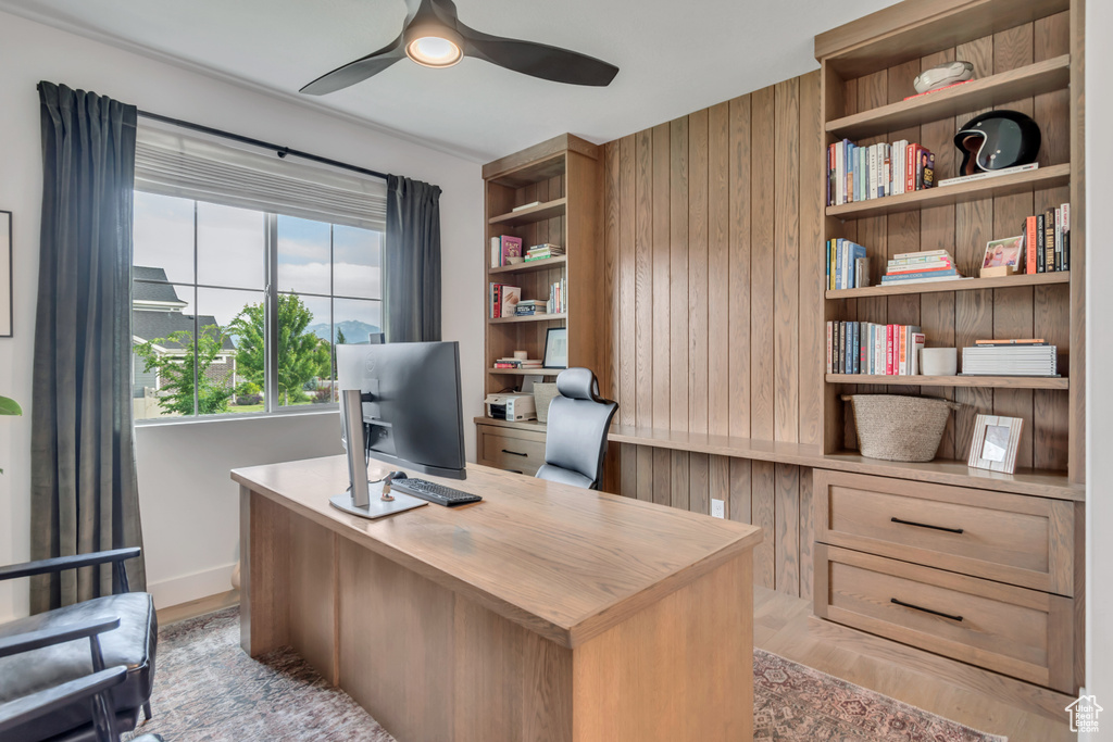 Home office with ceiling fan, wood walls, and light wood-type flooring